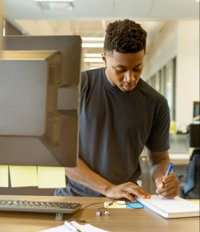 a young man taking notes at computer